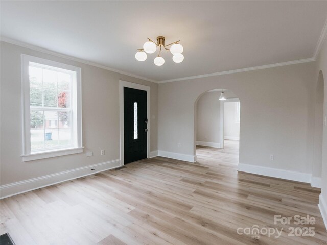 foyer entrance featuring arched walkways, ornamental molding, a chandelier, light wood-style floors, and baseboards