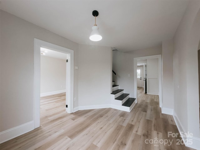 unfurnished room featuring light wood finished floors, stairs, and baseboards
