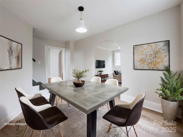 dining room with arched walkways, baseboards, and light wood-style flooring