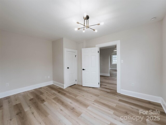 empty room featuring a chandelier, light wood finished floors, and baseboards