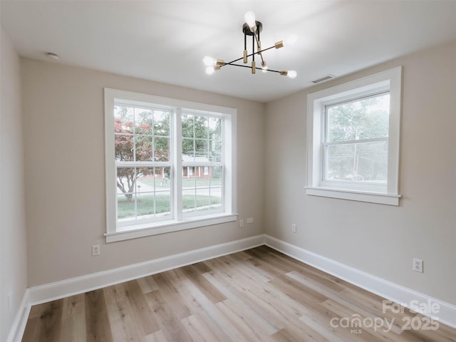 unfurnished room featuring a chandelier, plenty of natural light, light wood-style floors, and baseboards
