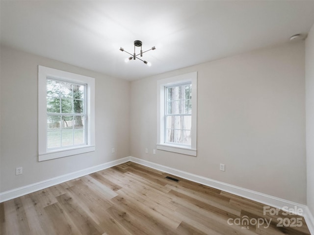 spare room featuring a chandelier, wood finished floors, and baseboards