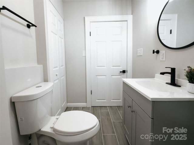 half bath with toilet, vanity, baseboards, and wood finish floors