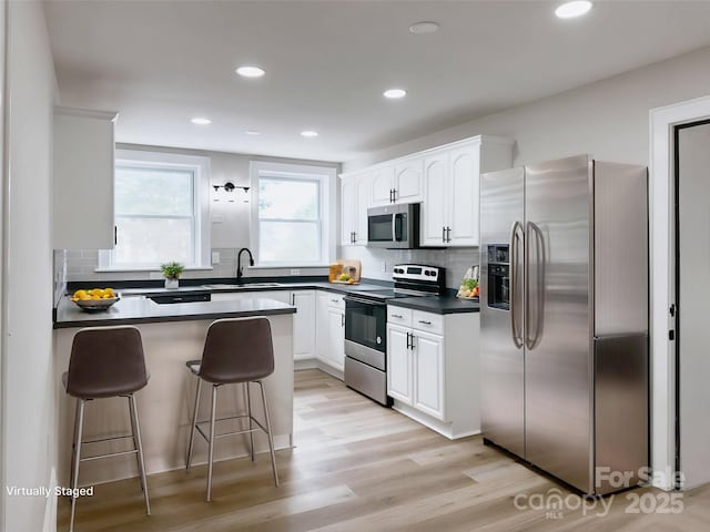 kitchen with stainless steel appliances, dark countertops, a sink, a breakfast bar area, and white cabinets