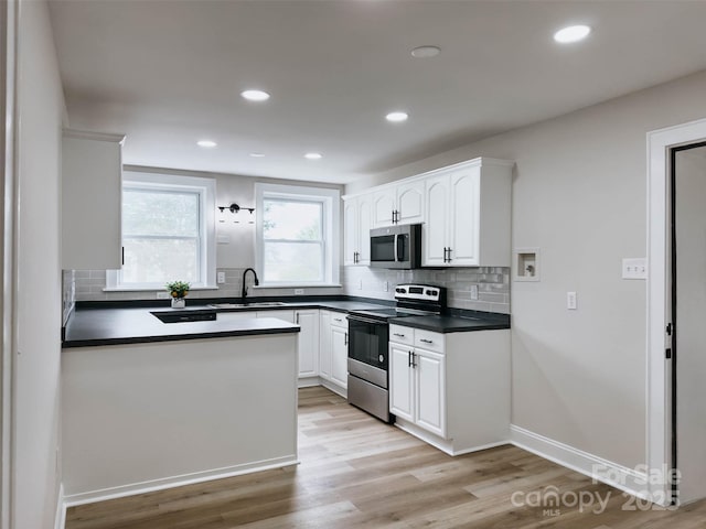 kitchen with stainless steel appliances, a sink, dark countertops, decorative backsplash, and light wood-style flooring