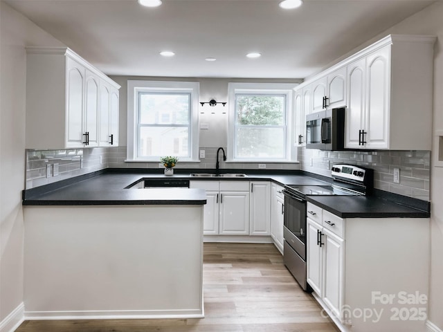 kitchen with a sink, stainless steel appliances, dark countertops, white cabinets, and recessed lighting