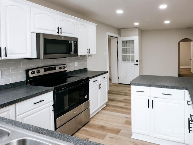 kitchen with stainless steel appliances, arched walkways, dark countertops, recessed lighting, and light wood-style floors