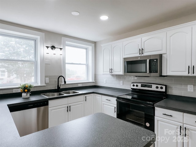 kitchen with appliances with stainless steel finishes, a sink, plenty of natural light, dark countertops, and recessed lighting