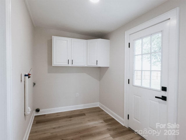 clothes washing area with cabinet space, light wood-style flooring, and baseboards