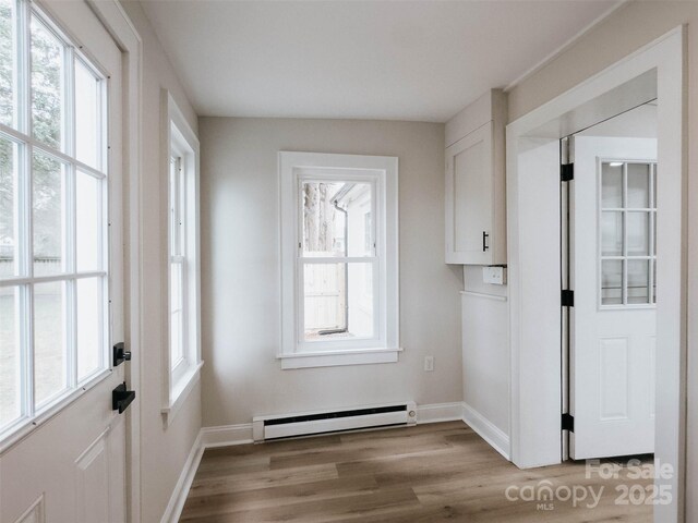 doorway to outside featuring a baseboard radiator, light wood-style flooring, healthy amount of natural light, and baseboards