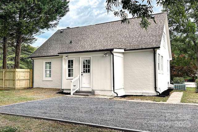 back of house with roof with shingles, fence, stucco siding, and central AC unit