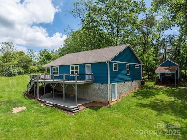 back of house with a wooden deck, a lawn, a shingled roof, an outdoor structure, and view of scattered trees