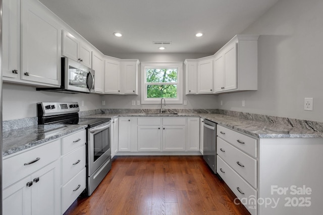 kitchen with appliances with stainless steel finishes, a sink, white cabinets, dark wood-style flooring, and recessed lighting