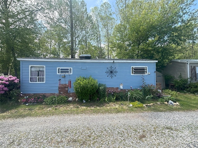 view of front facade with a wall mounted air conditioner and view of wooded area