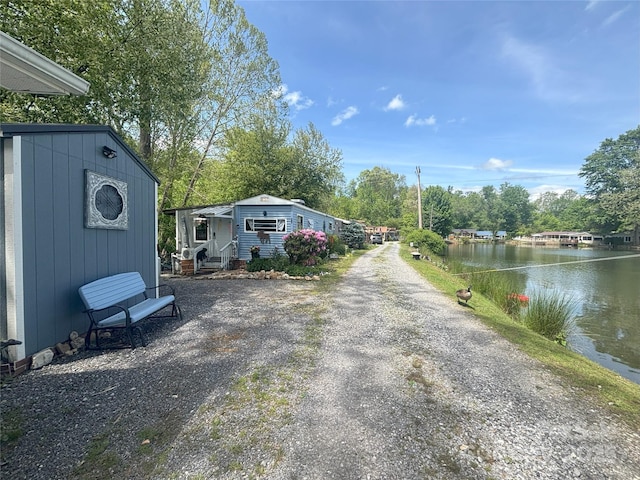view of dirt / gravel road with a water view and view of wooded area