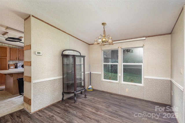 unfurnished dining area with vaulted ceiling, dark wood-style flooring, a chandelier, a textured ceiling, and crown molding