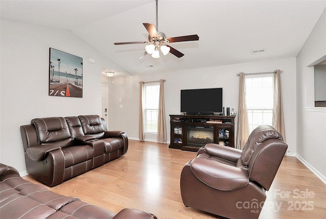 living area with light wood finished floors, ceiling fan, healthy amount of natural light, lofted ceiling, and baseboards