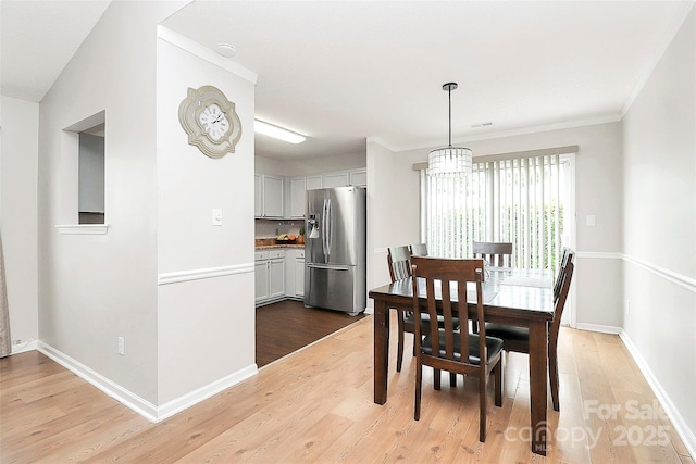 dining room with light wood-type flooring, a chandelier, baseboards, and crown molding