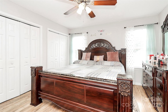 bedroom with light wood-style floors, multiple windows, multiple closets, and a ceiling fan