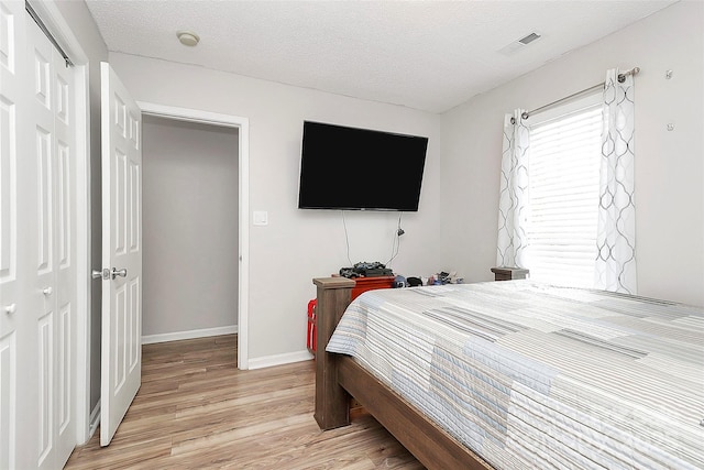 bedroom with light wood-type flooring, baseboards, and a textured ceiling