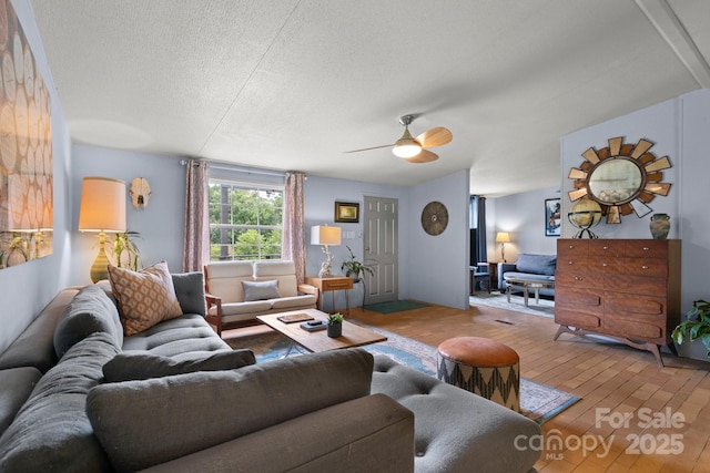 living room with hardwood / wood-style floors, a ceiling fan, and a textured ceiling