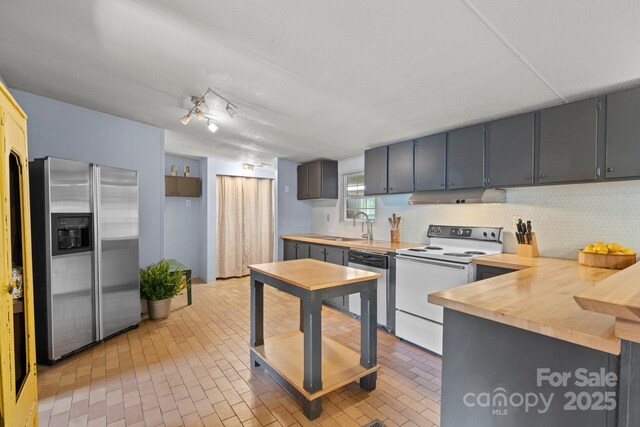 kitchen featuring appliances with stainless steel finishes, backsplash, a sink, and brick patterned flooring