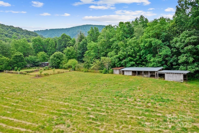 view of grassy yard with a wooded view, an outbuilding, a mountain view, and a pole building