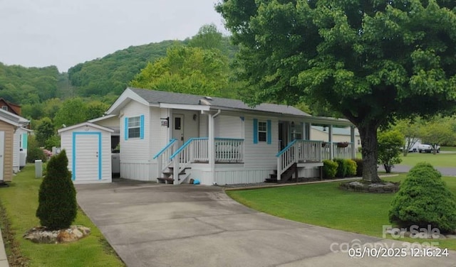 manufactured / mobile home with a porch, an outbuilding, driveway, a shed, and a front yard