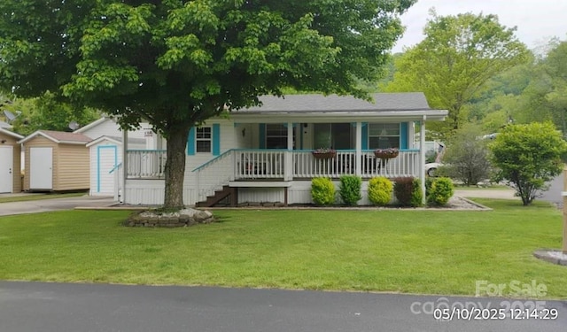 view of front of home featuring covered porch, a front yard, an outbuilding, a storage unit, and driveway
