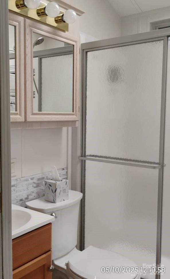 bathroom featuring vanity, a stall shower, decorative backsplash, and toilet