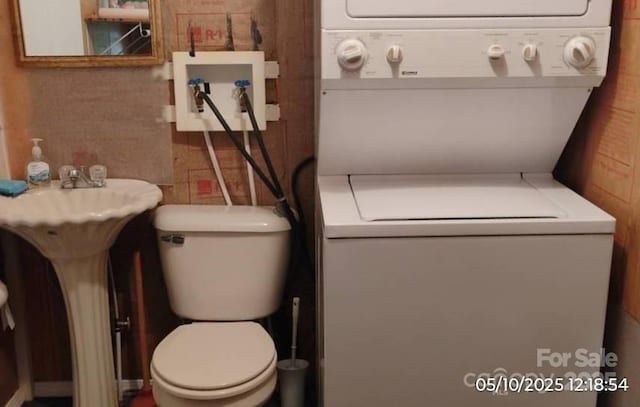 half bathroom with stacked washer / dryer and toilet