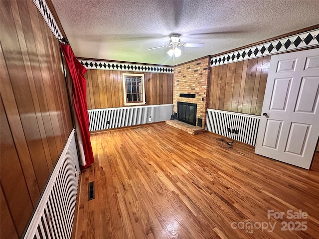 5495 Valley Run St, Hickory, NC 28601 - unfurnished living room with a textured ceiling, ceiling fan, wood finished floors, a fireplace, and wood walls