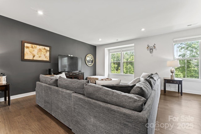 living room featuring healthy amount of natural light, dark wood-style flooring, baseboards, an accent wall, and recessed lighting