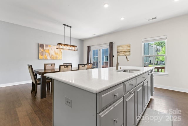 kitchen featuring gray cabinetry, a sink, dark wood-style flooring, baseboards, and an island with sink