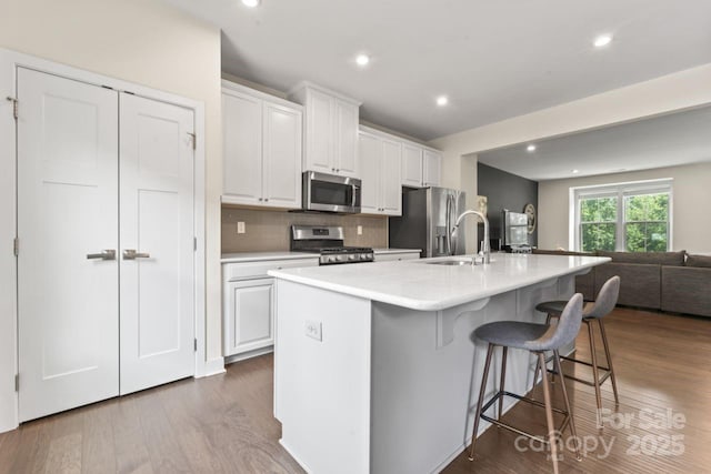 kitchen featuring appliances with stainless steel finishes, a sink, open floor plan, white cabinetry, and a spacious island