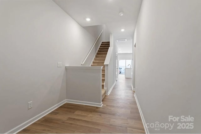 corridor featuring wood finished floors, baseboards, recessed lighting, and stairway