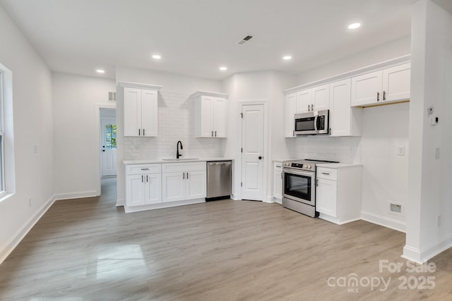 kitchen with appliances with stainless steel finishes, backsplash, a sink, light wood-style flooring, and light countertops