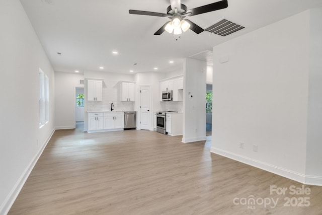 unfurnished living room featuring light wood-type flooring, recessed lighting, ceiling fan, a sink, and baseboards