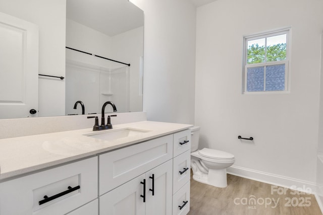bathroom with wood finished floors, baseboards, vanity, and toilet