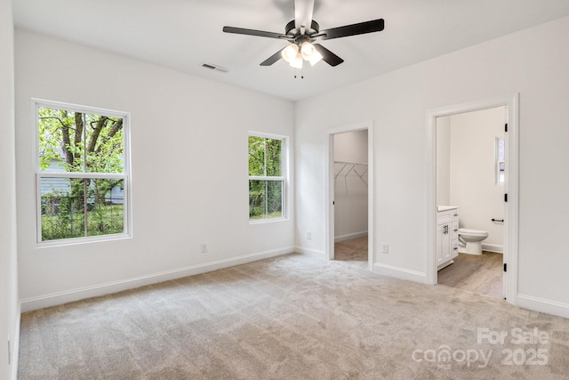unfurnished bedroom featuring multiple windows, light carpet, a spacious closet, and baseboards