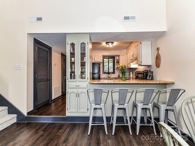 100 Willow Run Dr Unit 26, Gastonia, NC 28056 - kitchen featuring dark wood finished floors, a breakfast bar area, glass insert cabinets, backsplash, and a peninsula