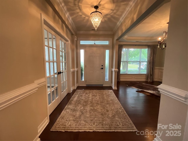 foyer with dark wood-type flooring, crown molding, french doors, a chandelier, and a wainscoted wall