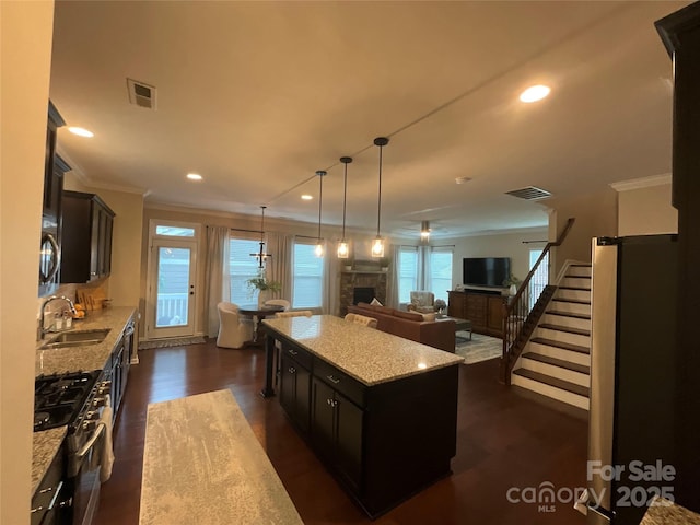 kitchen featuring gas range, a sink, a center island, crown molding, and light stone counters