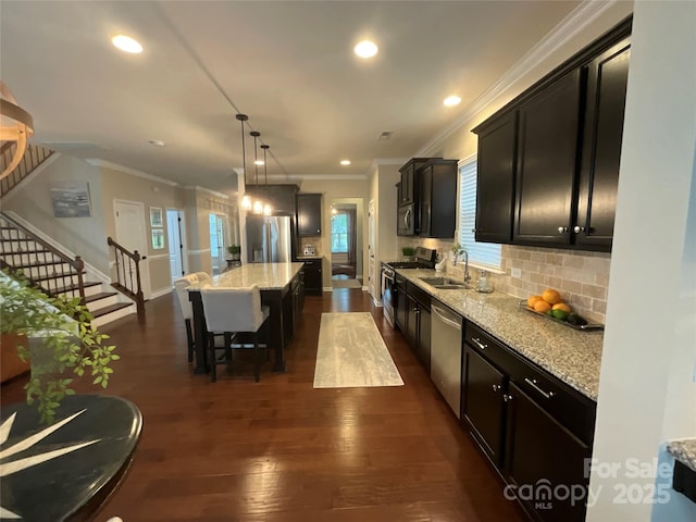 kitchen with appliances with stainless steel finishes, a sink, ornamental molding, dark wood-style flooring, and a kitchen island