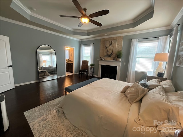 bedroom featuring a raised ceiling, wood finished floors, a fireplace, ornamental molding, and baseboards