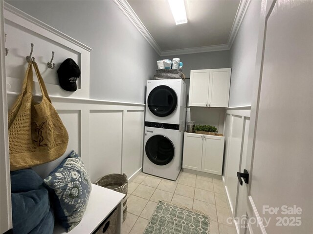 laundry room with estacked washer and dryer, cabinet space, a decorative wall, crown molding, and light tile patterned flooring
