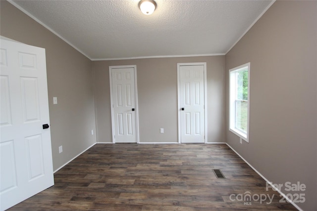 unfurnished bedroom featuring multiple closets, ornamental molding, a textured ceiling, dark wood-style floors, and baseboards