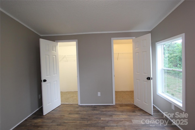unfurnished bedroom featuring a spacious closet, crown molding, wood finished floors, a textured ceiling, and a closet