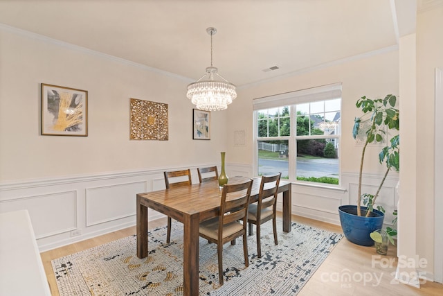 1104 Snowbird Ln, Waxhaw, NC 28173 - dining space featuring light wood-style floors, a chandelier, ornamental molding, a decorative wall, and wainscoting
