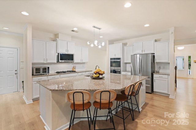 1104 Snowbird Ln, Waxhaw, NC 28173 - kitchen with stainless steel appliances, white cabinets, a large island, light wood finished floors, and recessed lighting
